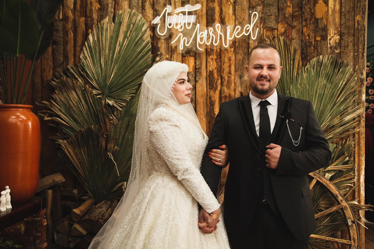 A newlywed couple poses elegantly indoors in wedding attire.